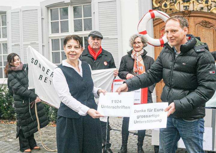 Tobias Ammann übergibt die Unterschriften an Elisabeth Heer Dietrich, im Hintergrund dazwischen Andreas Bammatter und Juliana Weber Killer. Bild da.